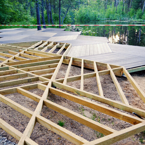 Walking area on screw piles, wooden frame, plastic terrace board on pond shore in park, construction site